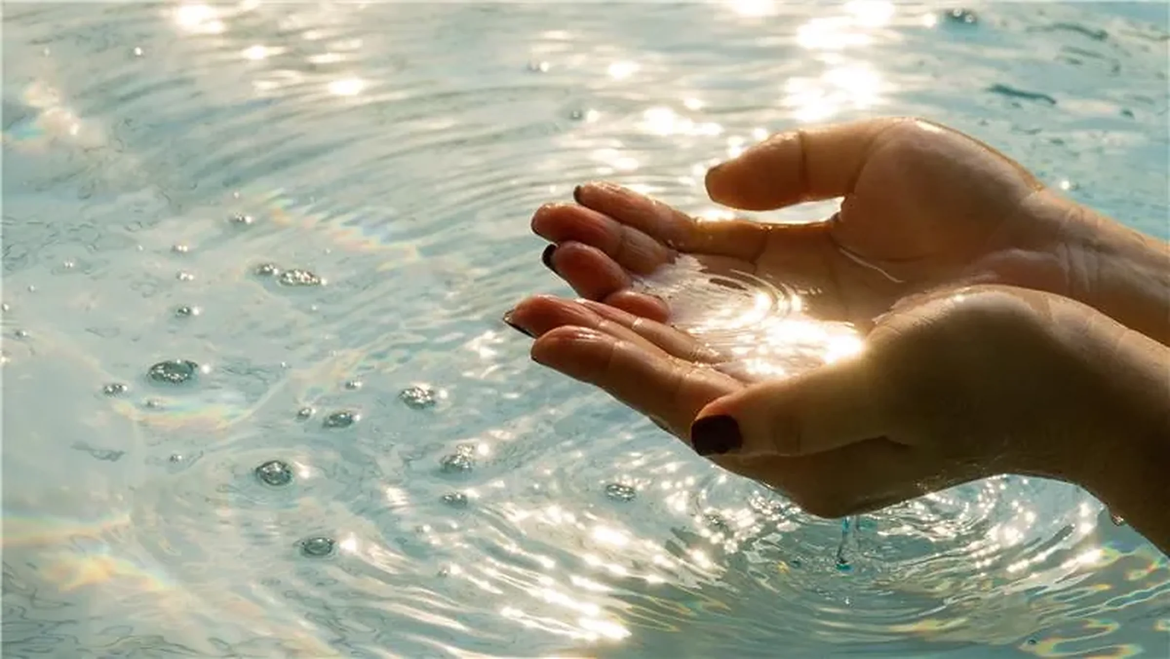 Cupped hands holding clean water, sunlight glinting on the rippled surface